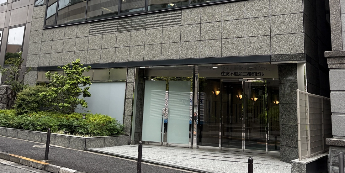 「住友不動産三番町ビル」の石造り外壁とガラス扉が並ぶオフィスビル入口、前に歩道と植栽が配置された外観